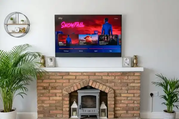 TV wall mounted above fireplace with log burner in Colchester